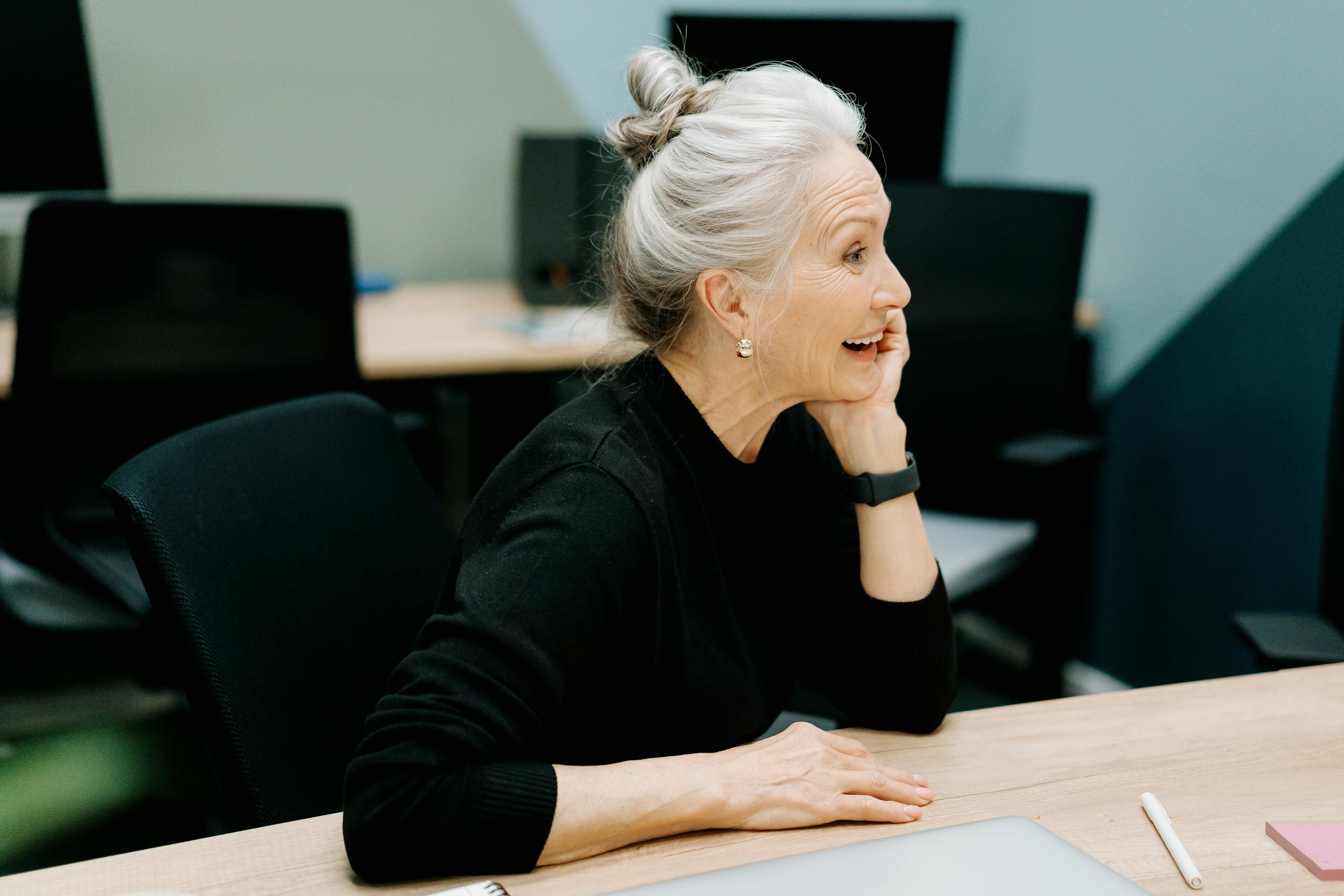 Senior businesswoman smiling at a desk in a modern office, conveying positivity and leadership.